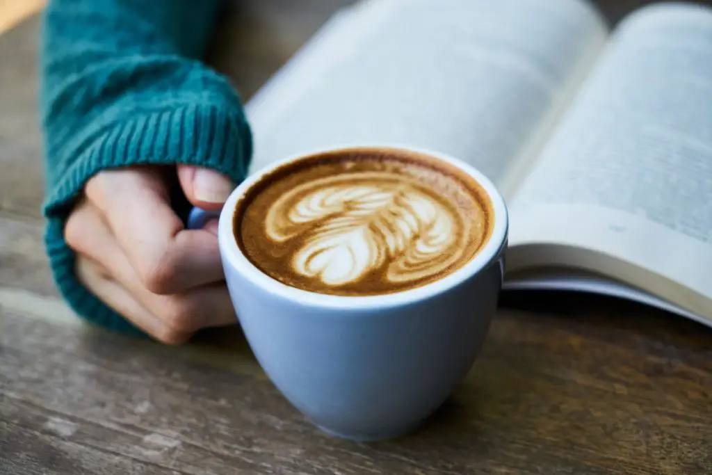 A woman holding a latte as she reads a book