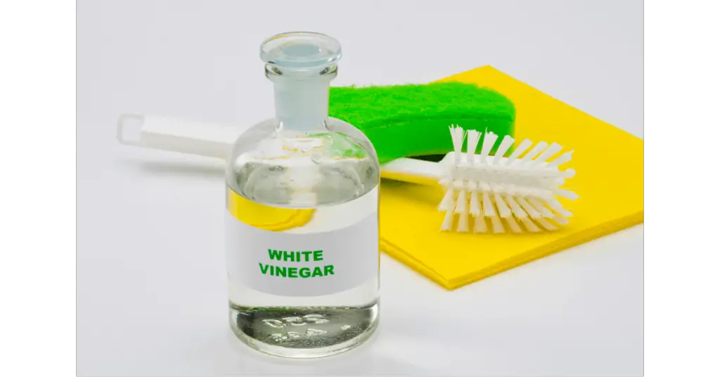 A bottle of vinegar in front of cleaning brushes and sponges