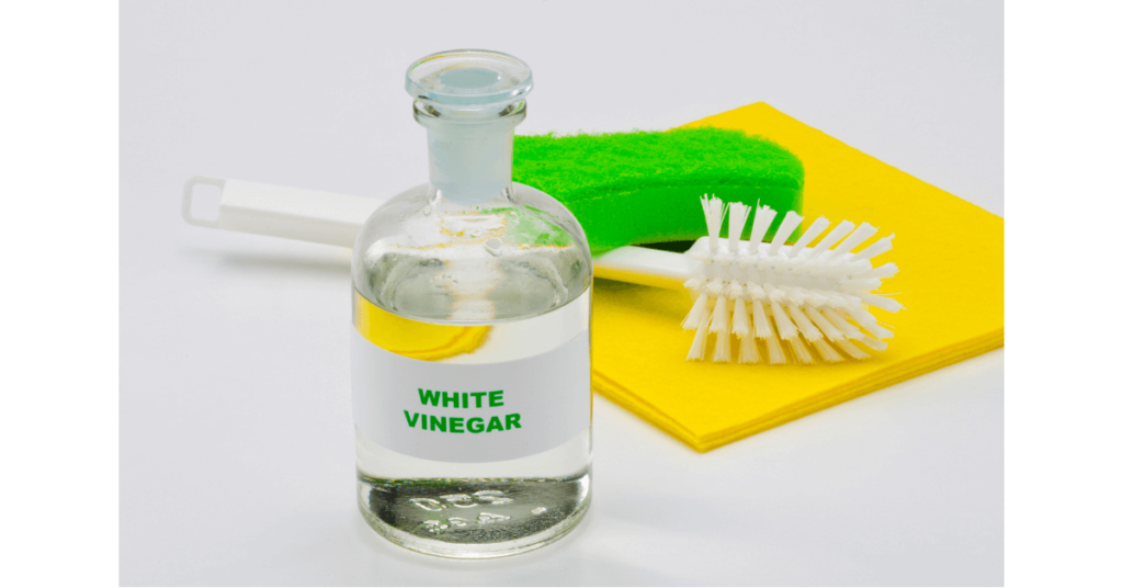 A bottle of vinegar in front of cleaning brushes and sponges