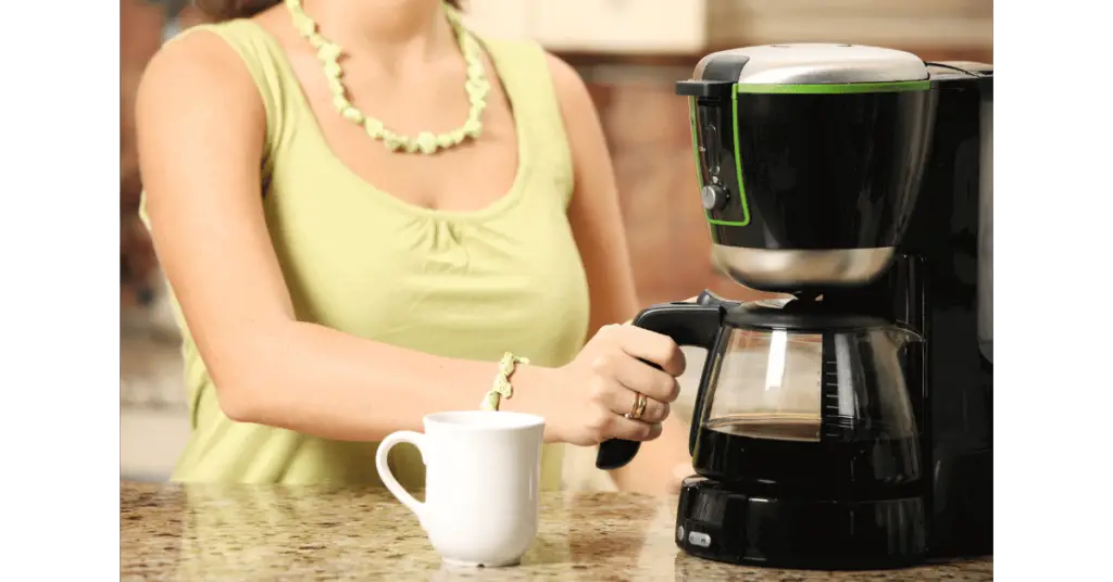 A woman about to pour coffee from a drip coffee maker
