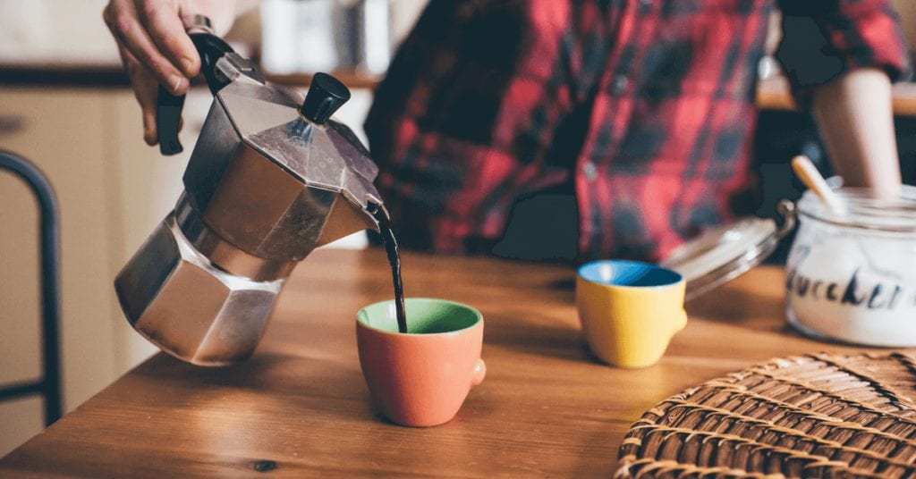 A person pouring their Moka pot coffee into a mug