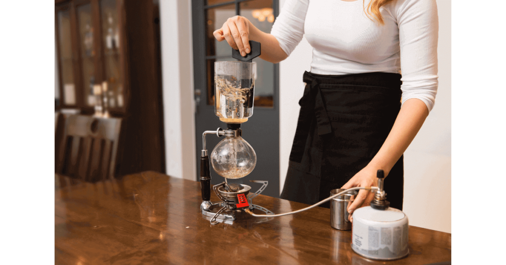 A woman using a siphon coffee maker to brew coffee