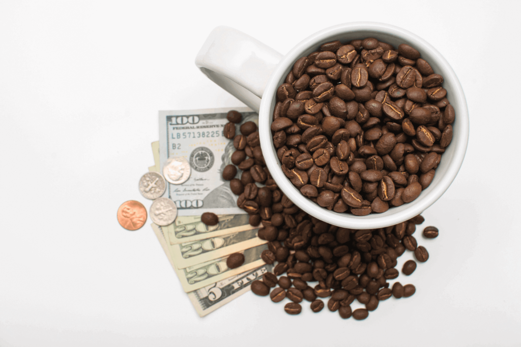 A cup of coffee beans on top of some dollar bills, illustrating what a cup of coffee costs